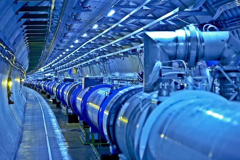 The long curving atom tunnel at the LHC during construction, lit in blue and yellow.