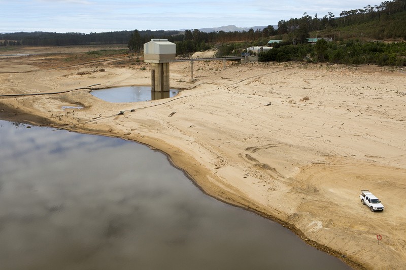Low levels of water in Theewaterskloof Dam and Reservoir, with a car parked on the dried out bed.
