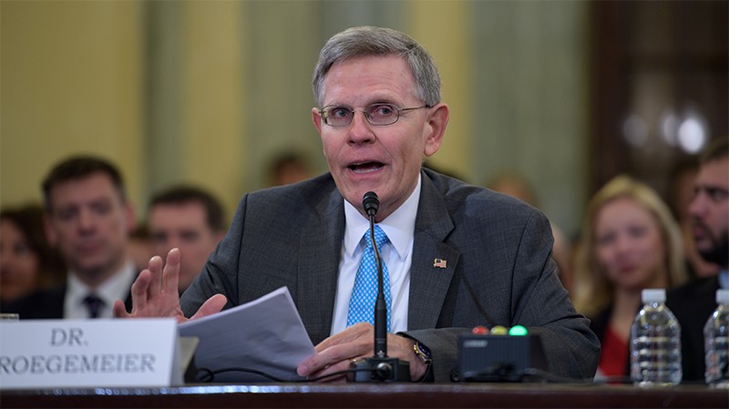 Kelvin Droegemeier, seated, talks into a microphone whilst holding notes at the Russell Senate Bldng, Washington