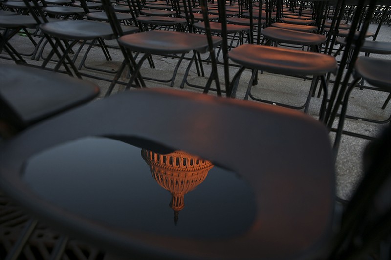 U.S. Capitol building is reflected in a water puddle on a chair arranged for an audience