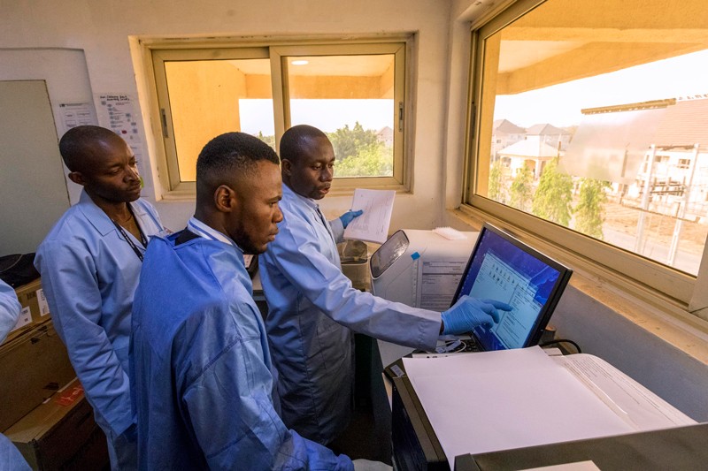 Three workers in blue lab coats stand around a computer in a lab at the Nigeria Center for Disease Control