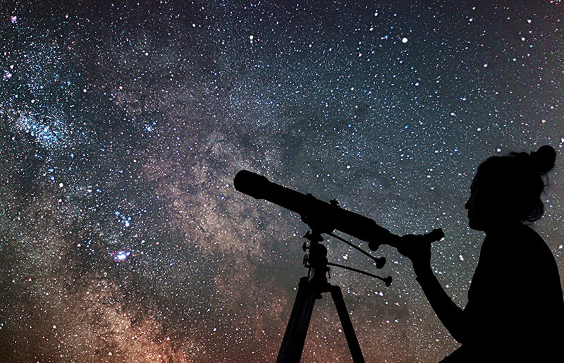 Woman with a telescope in front of a field of stars.