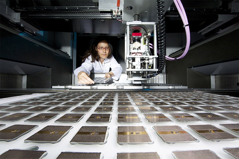 Maike Wiesenfarth sits behind a machine used to make solar cells and rows of assembled solar cells.