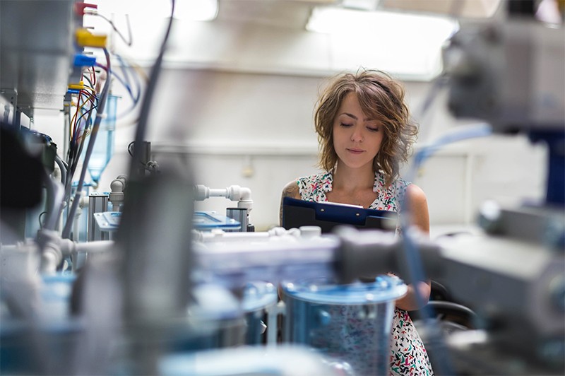 A female scientist examines printed data whilst working on machines in a laboratory
