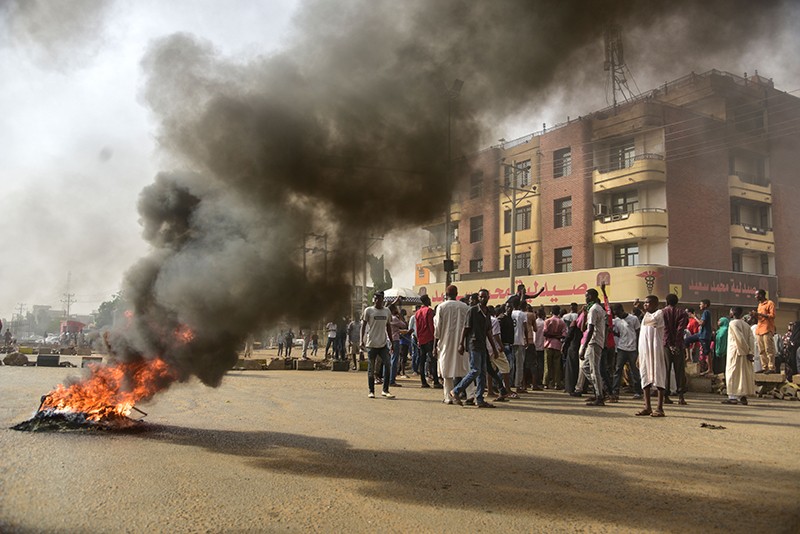 Sudanese protesters walk past burning tyres in Omdurman