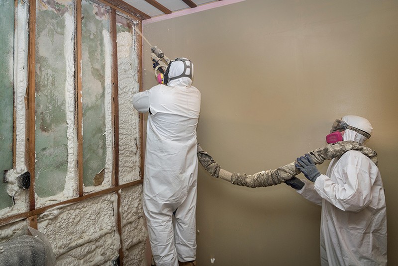 Workers spraying open-cell foam insulation on interior walls ofa home