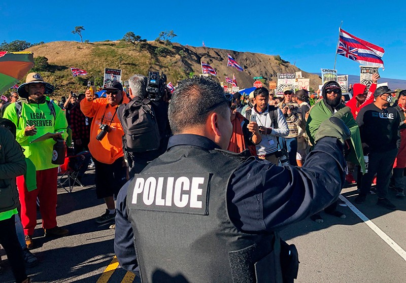 police officer gestures at demonstrators blocking a road at the base of Hawaii's tallest mountain