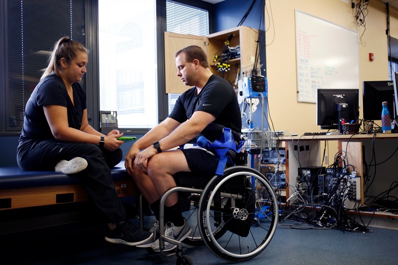 Katie Pfost (Left) controls Rob Summers' spinal stimulator with a tablet before conducting treadmill locomotive training