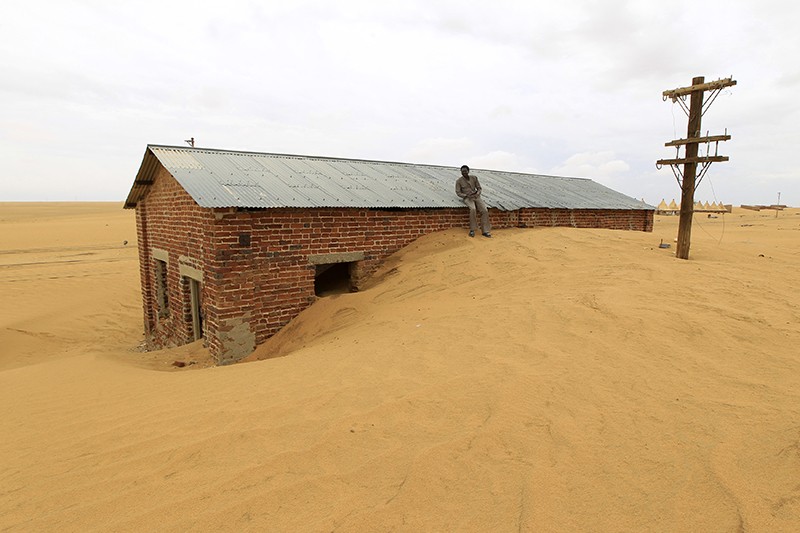 A man waits at the Ogrein Railway Station, with desert encroachment shown, in Sudan