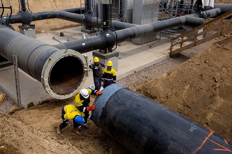 Workers guide a section of pipe before connecting to a gas pipeline control station on the European Gas Pipeline Link site