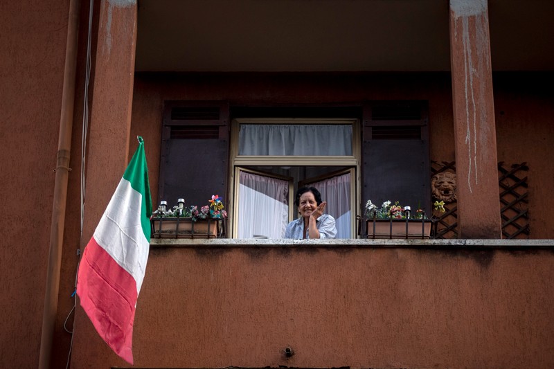 A woman with the Italian flag looks out of her balcony, Rome