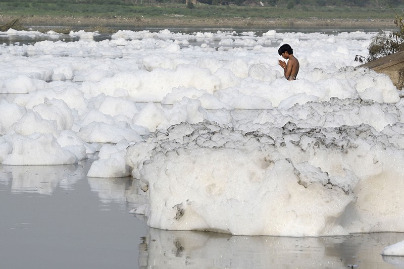 An Indian Hindu devotee prays amongst foam in the polluted Yamuna river in New Delhi, in 2017.