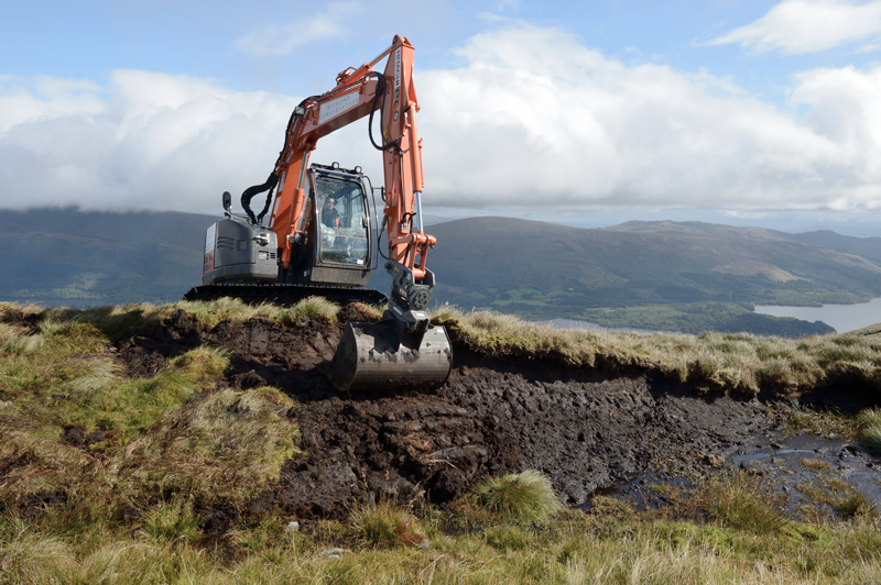 An excavator digs up sections of peat on an exposed peat hag