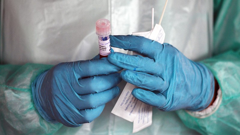 Two hands in blue gloves holding testing tube with lid.