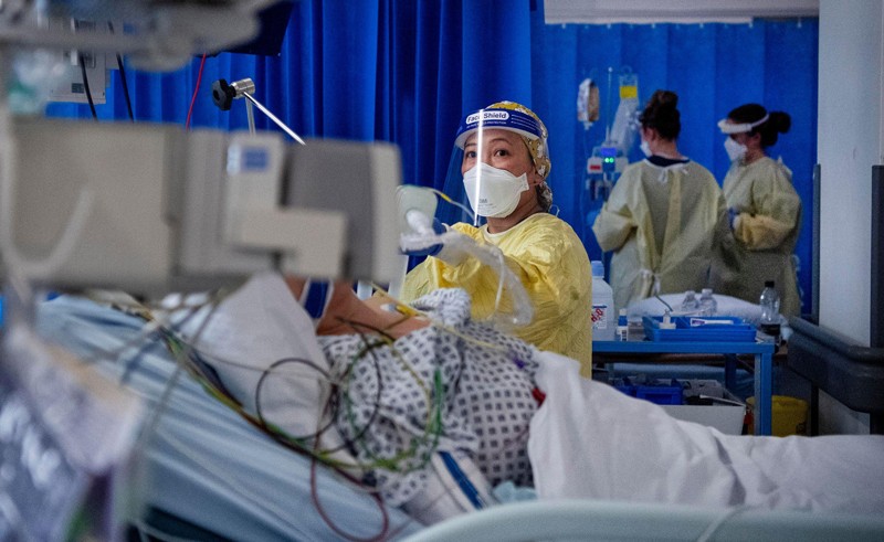 A nurse wearing a face mask and face shield attends to a patient in an intensive care unit