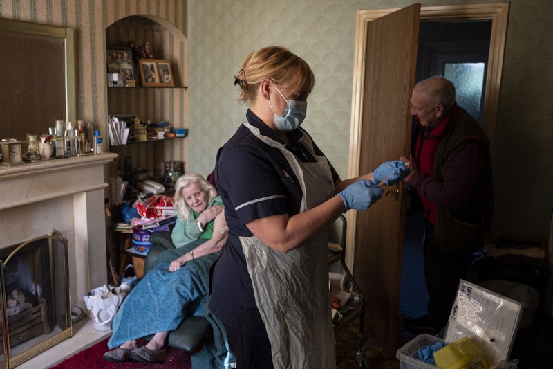 Um profissional de saúde prepara uma vacina Oxford / Astra Zeneca para uma mulher idosa em sua casa no Reino Unido