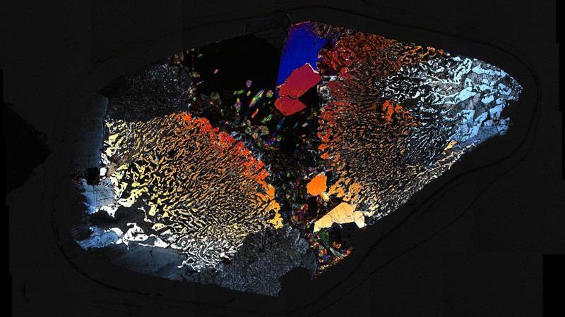 A transmission light micrograph of a rock thin section: a pattern of colours on a dark background.