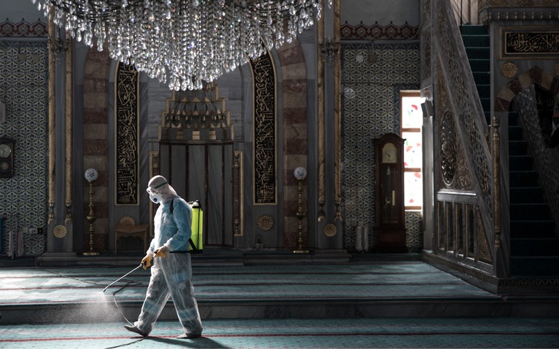 A person in protective clothing sprays disinfectant in a lavishly decorated room with a chandelier.
