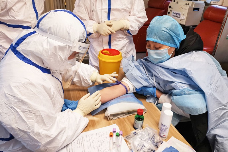 A person donating plasma surrounded by medical workers in prote