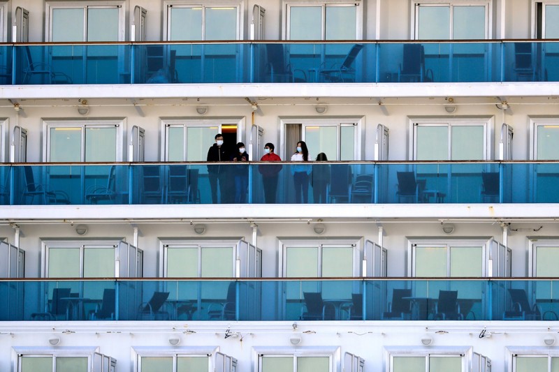 People in facemasks stand on balconies separated by partitions, surrounded by many empty balconies.