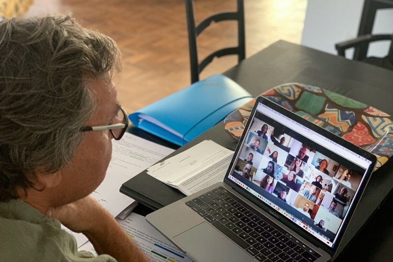 A man looking at a laptop showing the faces of meeting attendees.