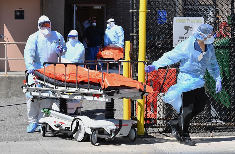 People in protective equipment push a cart with a body on top