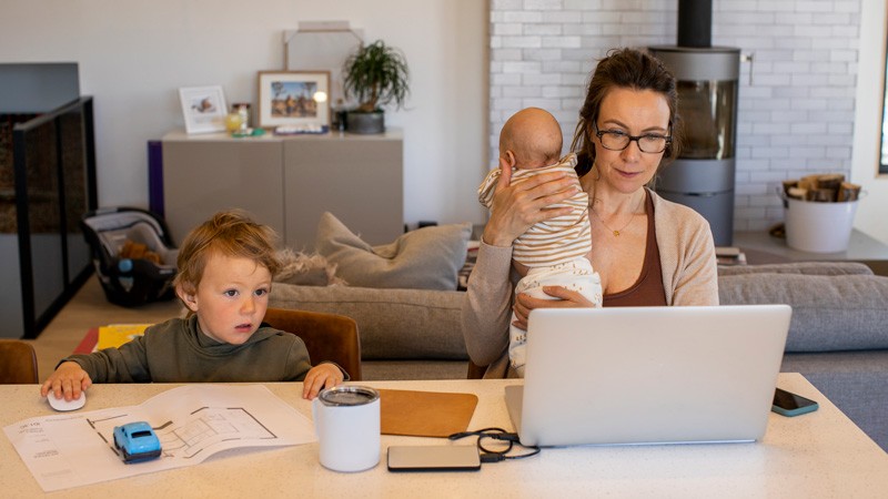 A mom trying to work from home while holding her daughter and watching her son during the COVID-19 home quarantine.