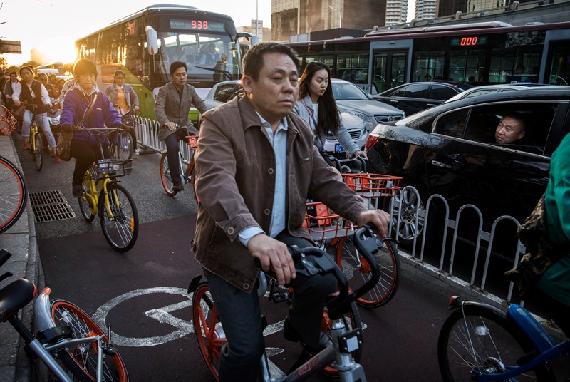 A man watches from a car as Chinese commuters crowd the bicycle lane as they ride bike shares during rush hour