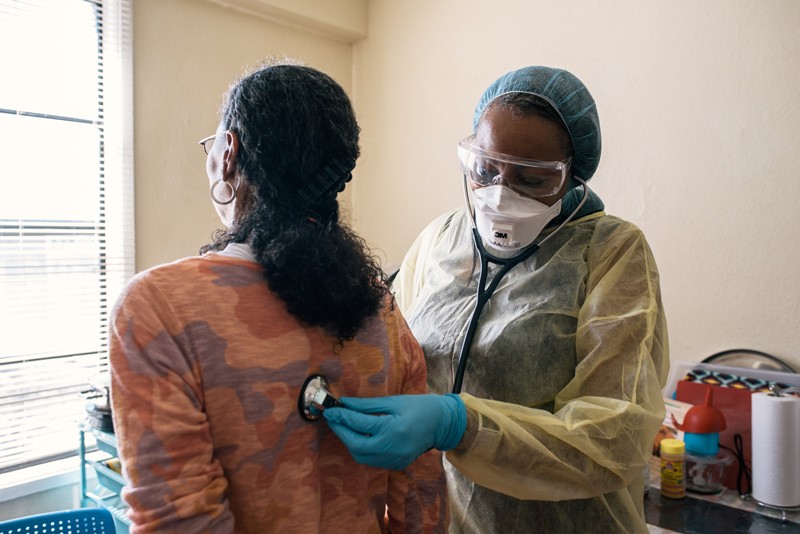 A respiratory therapist in protective clothing uses a stethoscope to listen to the lungs of a patient with asthma