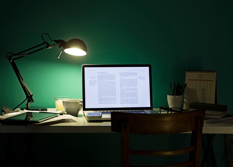 Computer and phone illuminated by desk lamp at night