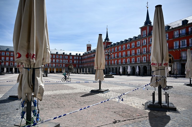 A cyclist rides their bike next to the terrace of a closed restaurant in Madrid's Plaza Mayor