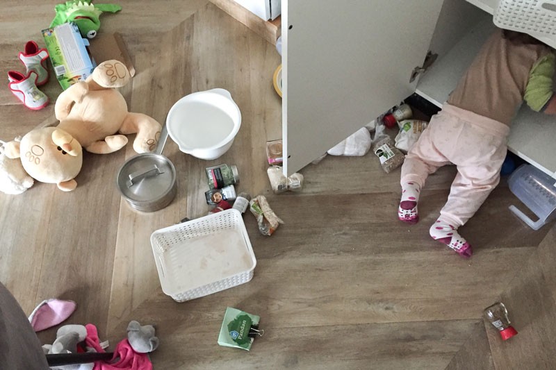 A young child rooting in an open cupboard, surrounded by mess.