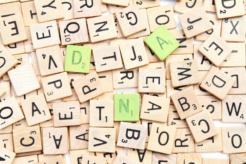 Scrabble tiles with three painted green letters spelling DNA scattered on a pile of random letters