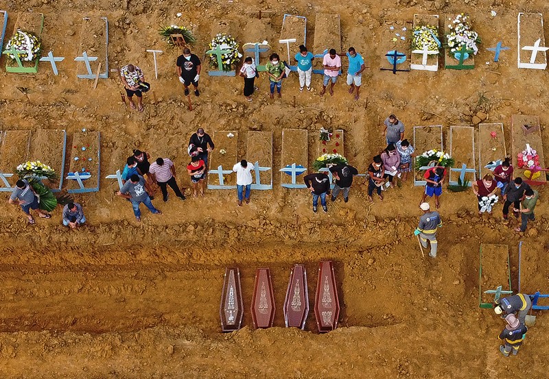 Aerial picture of people attending the burial of four coffins at an area where many new graves have been dug up