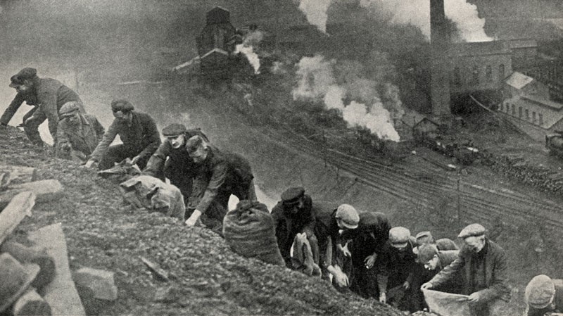 A line of unemployed men carrying sacks search for lumps of coal on a slag heap in South Wales