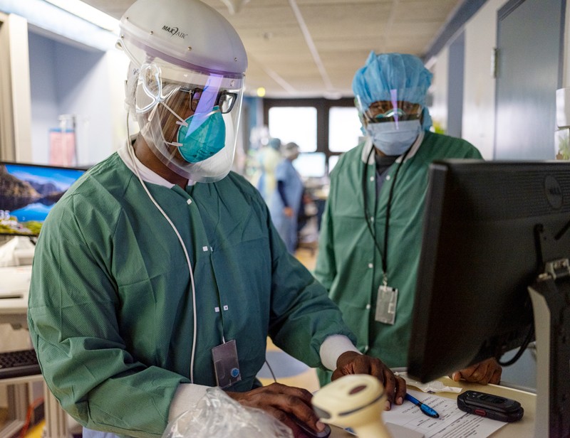 Medical staff wearing protective clothing and a ventilator looking at a computer monitor in a hospital intensive care unit