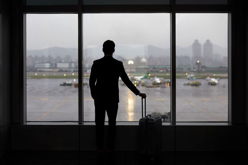 A man with luggage looking through a window at an airport