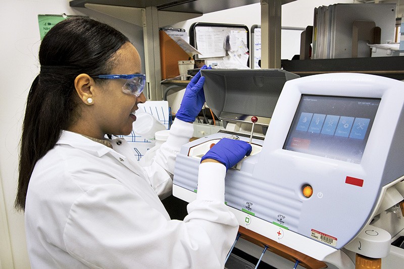 Technician loading DNA samples into a desktop genomic sequencing machine