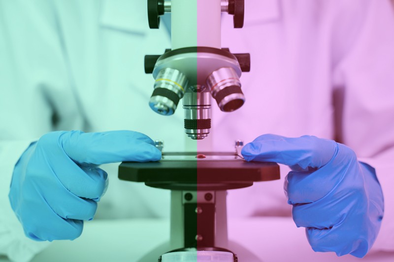 Researcher in a lab coat and gloves uses a microscope. The picture has a green tint on the left and a red tint on the right.