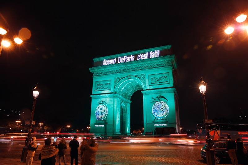 The Arc de Triomphe is illuminated in green with the words "Paris Agreement is Done"