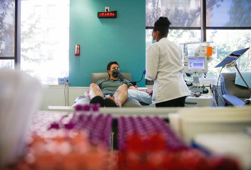 A medial worker in a white coat talks to a patient in a chair as he donates convalescent plasma