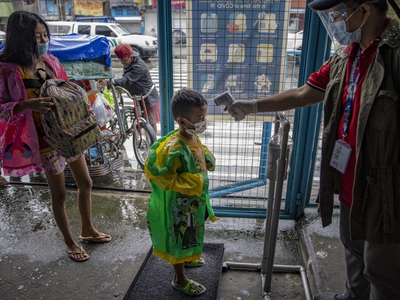 A boy has his temperature checked as a measure against COVID-19, as they arrive at an evacuation center, Manila.