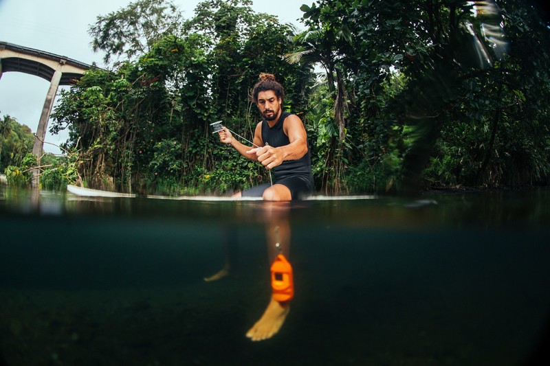 Cliff Kapono on his surfboard testing the water with a measuring tool.