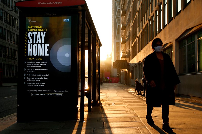 A pedestrian wearing a face mask walks past a digital display describing COVID measures.