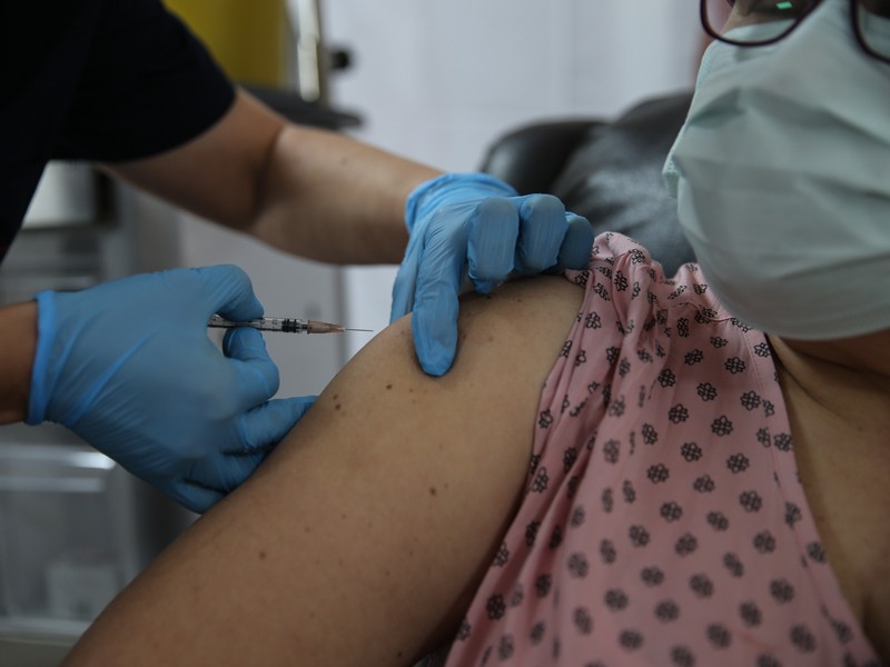 A health-care worker injects a masked person with a vaccine.