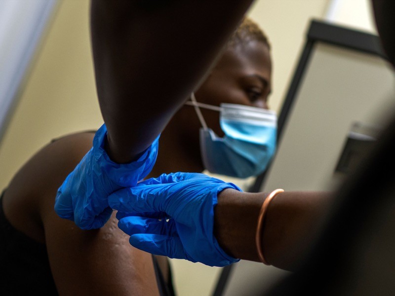 A woman wearing a mask is given a vaccination by a health worker in blue gloves.