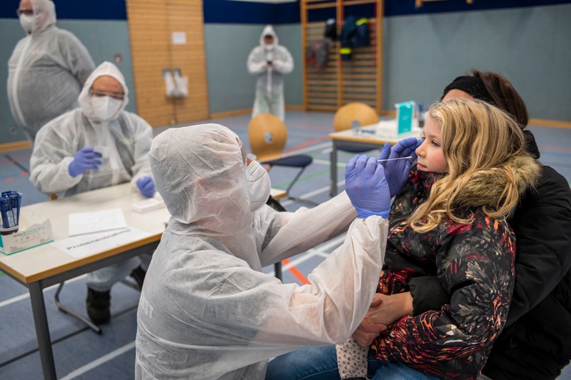 A health-care worker takes a nasal swab from a girl being held in her mother's arms.