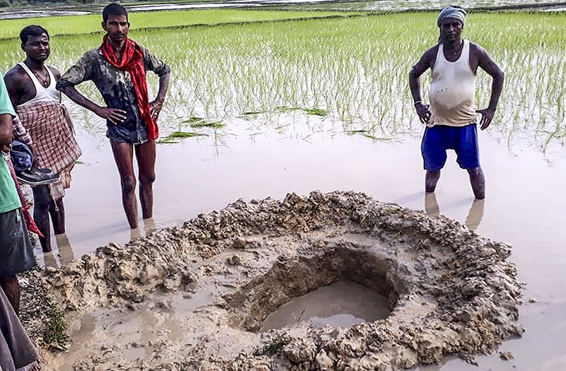 Farmers pose around the crater of a 10 kg meteorite that crashed in a field at Mahadeva village in India