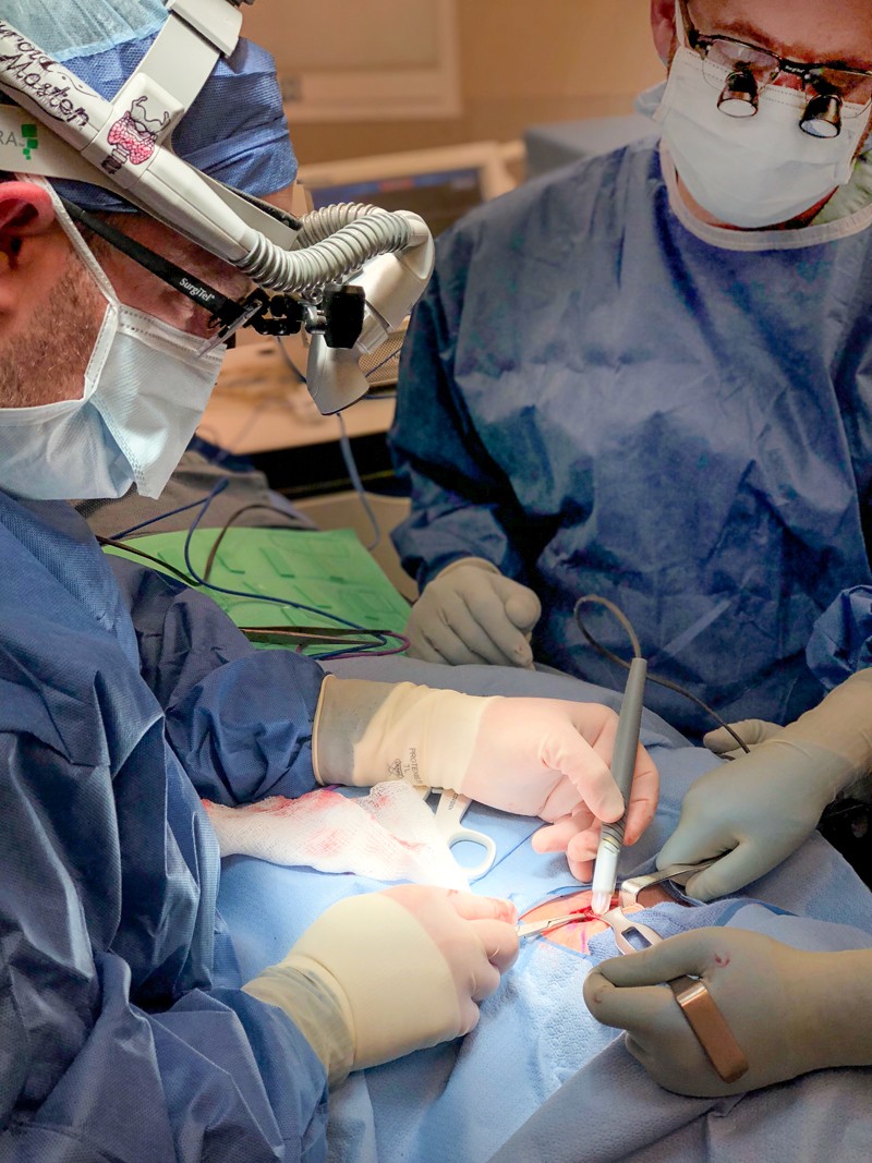 Two surgeons operate on a patient using a pen-like electronic device to analyse tissue