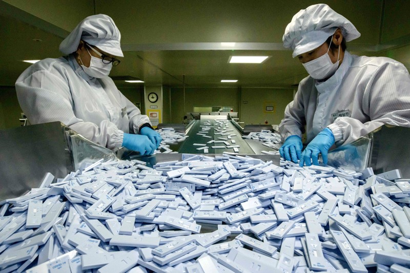 Workers inspect small plastic COVID-19 testing devices on a conveyor belt at a production facility in South Korea